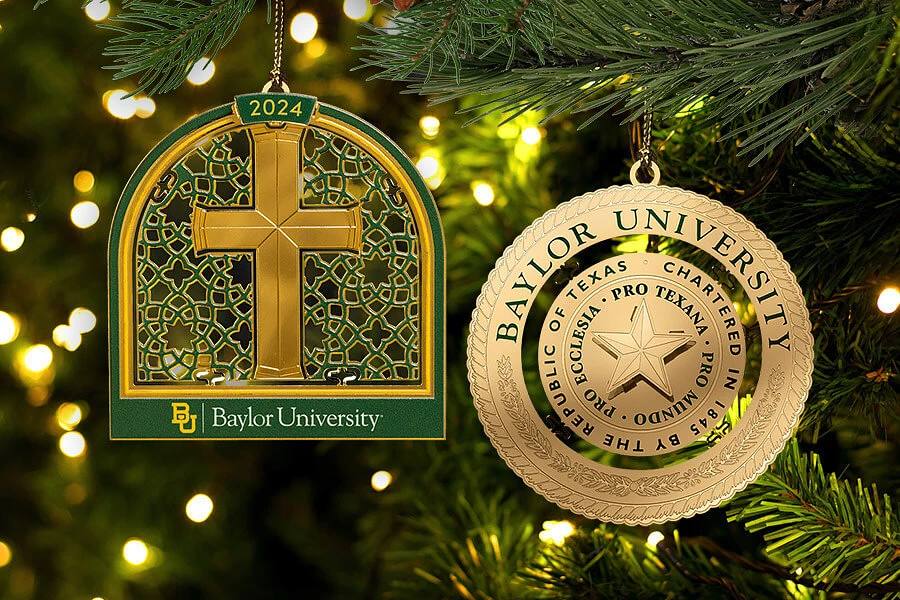 Two Baylor University ornaments, one featuring a cross and the other a medallion with the university seal, hang on a Christmas tree.